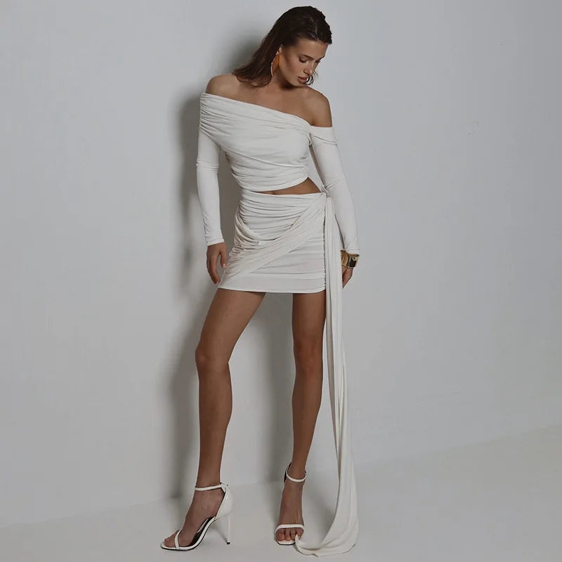 Woman wearing a white off-shoulder dress with long sleeves against a plain background