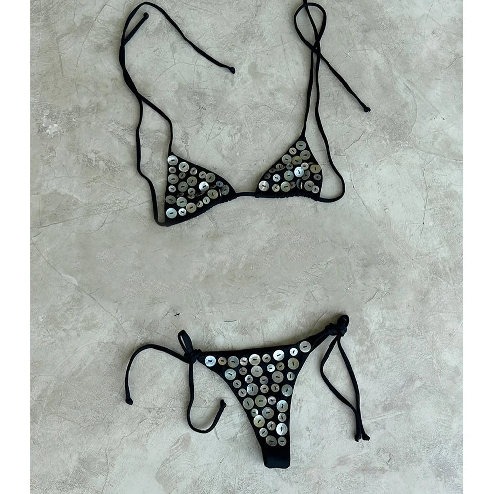 Black embellished bikini set on a grey concrete-like surface.