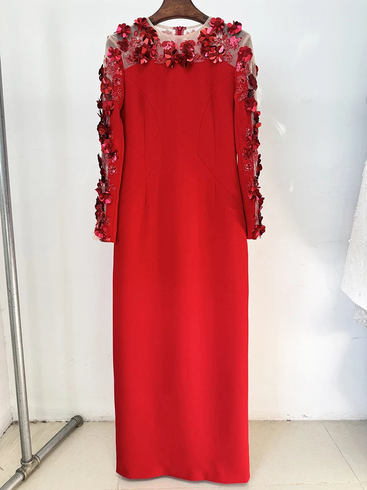 Red dress with floral embellishments on a hanger against a white wall.