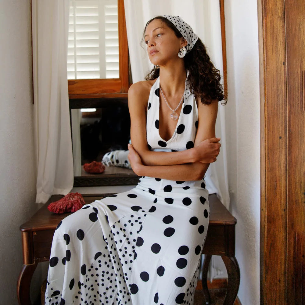 Woman in a white dress with black polka dots sitting on a wooden bench.