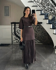 Woman taking a mirror selfie in a dark brown dress with a pleated skirt in a staircase setting.