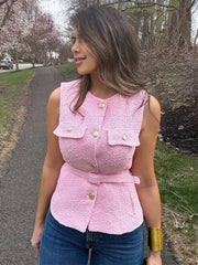 Woman wearing a pink textured top with buttons outdoors on a path with trees and grass.