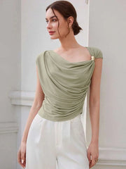 Woman wearing a green top with a draped design and white pants against a light background