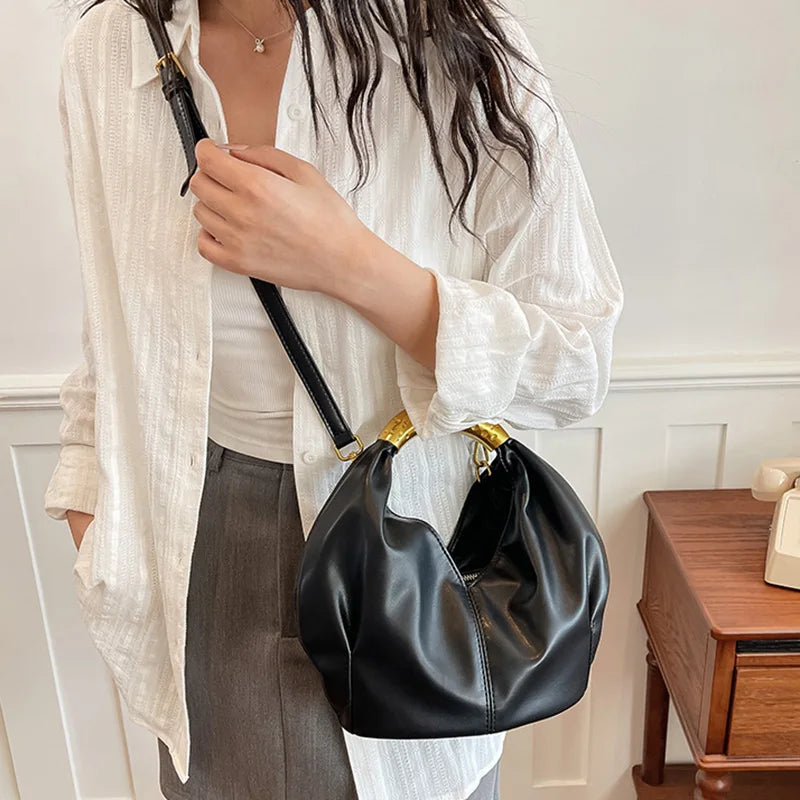 Person wearing a white shirt and grey pants, carrying a black soft PU leather dumpling shaped handbag with a metal handle across the body.