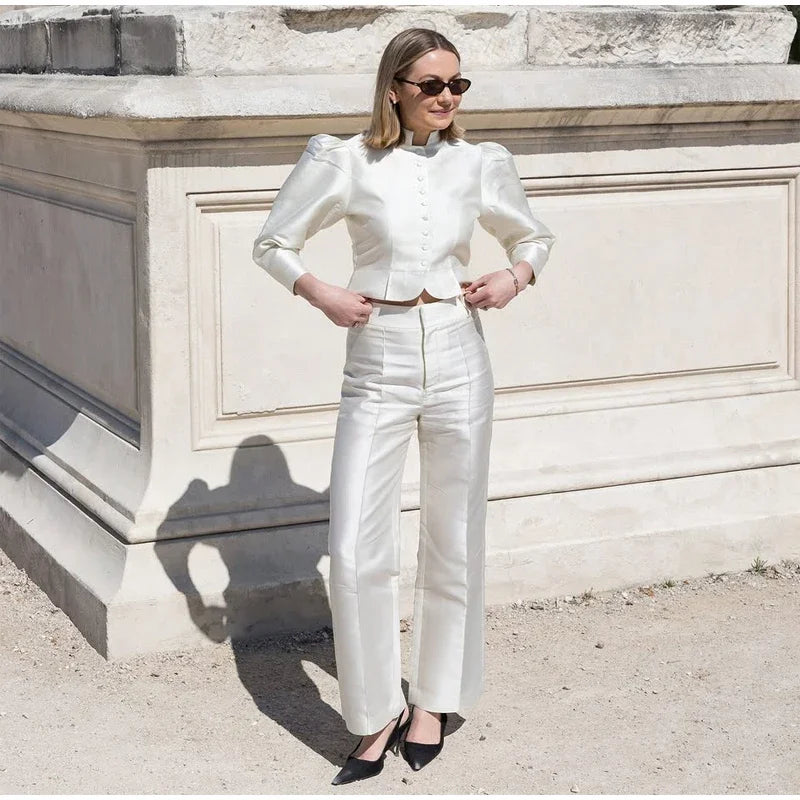 Woman in a white outfit standing in front of a stone wall.