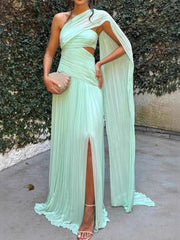 Woman wearing a light green evening gown with a slit, standing against a textured wall.