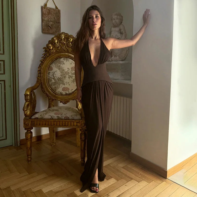 Woman in a brown dress standing in a room with a gold chair and decorative wall.