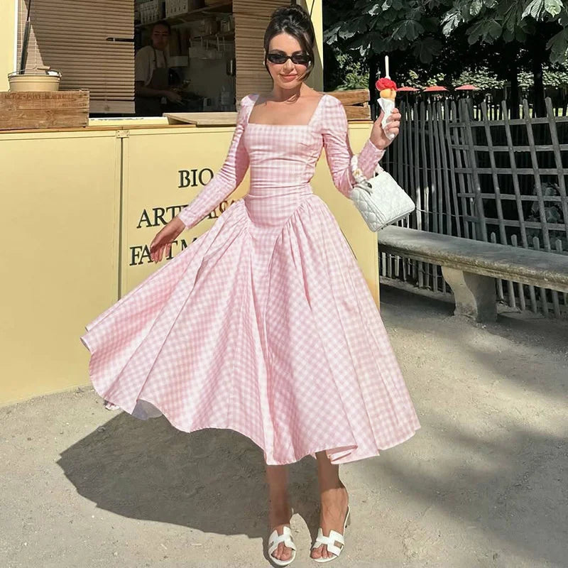 Woman in a pink checkered dress holding an ice cream cone outdoors.