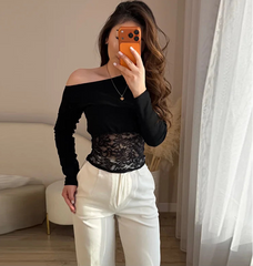Woman taking a mirror selfie wearing a black off-shoulder top with lace detail and white pants.