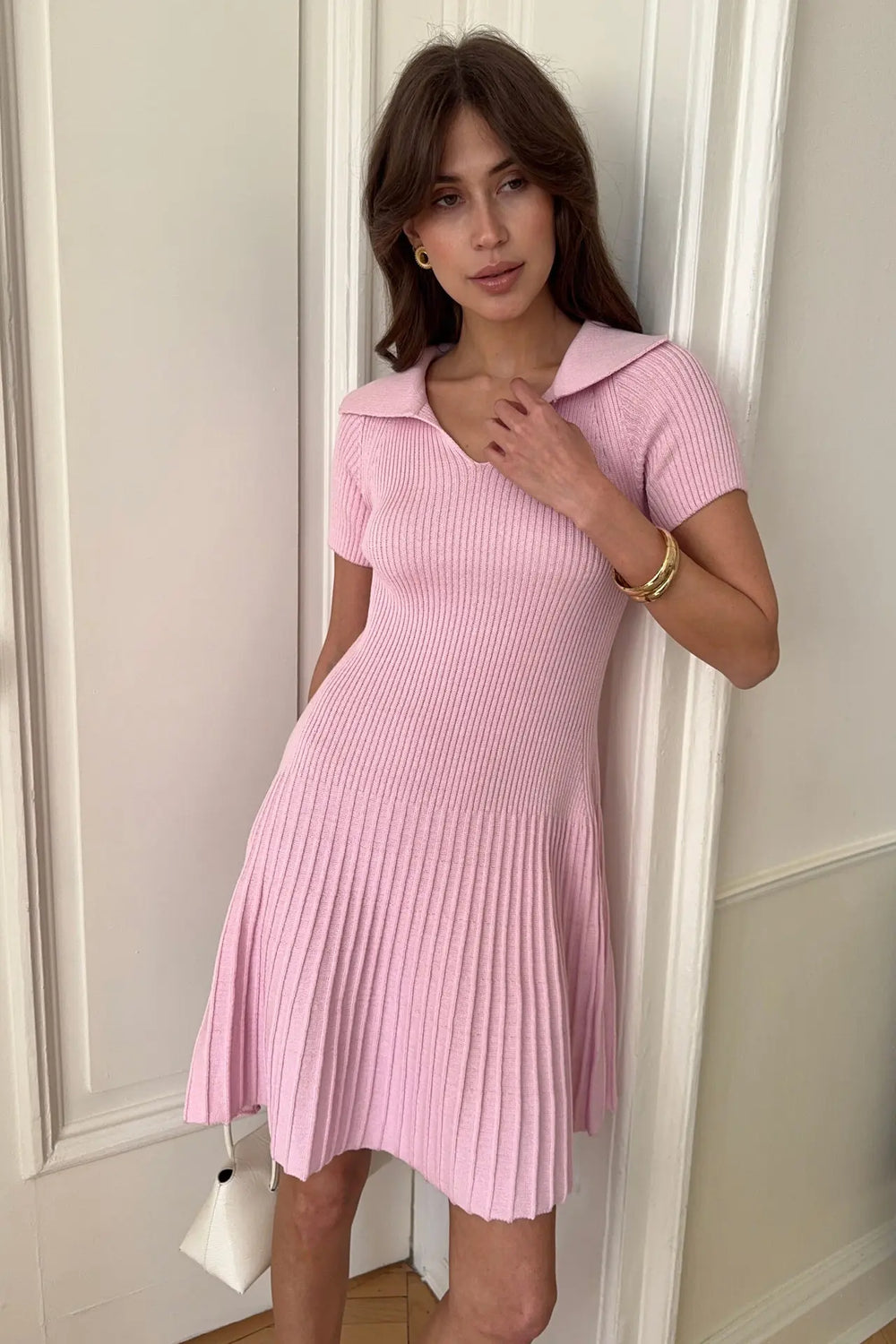 Woman wearing a pink ribbed dress standing against a white wall.