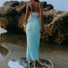 Woman in a light blue dress with floral top standing on a rocky beach.
