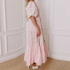 Woman wearing a pink floral dress standing against a white paneled wall.
