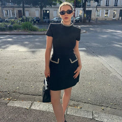 Woman in a black dress with embellishments standing on a street.