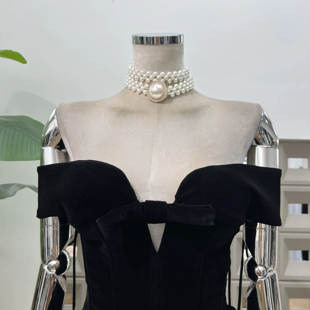 Mannequin wearing a black off-shoulder top with a pearl necklace against a neutral background