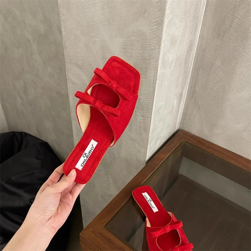 Red sandal held by a hand with a mirror reflection on a neutral background