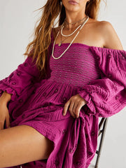 Woman wearing a magenta off-shoulder dress with long sleeves on a plain background