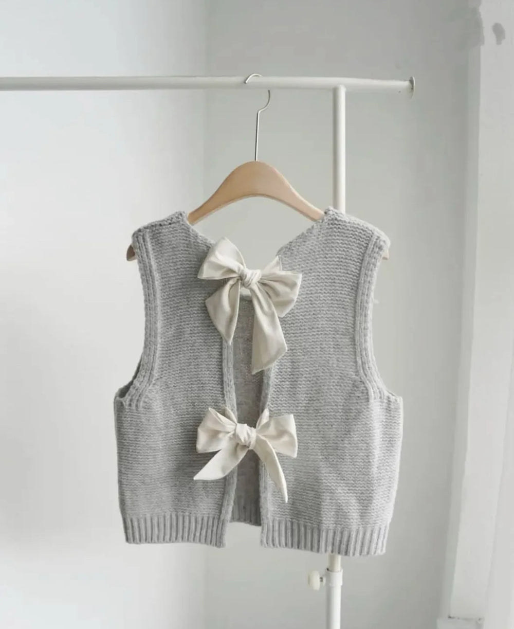 Gray knitted vest with white bows on a hanger against a white background