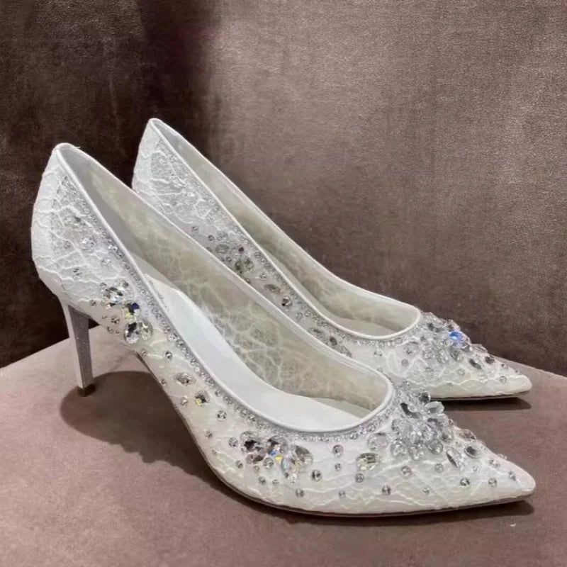 White high-heeled shoes with crystal embellishments on a brown surface
