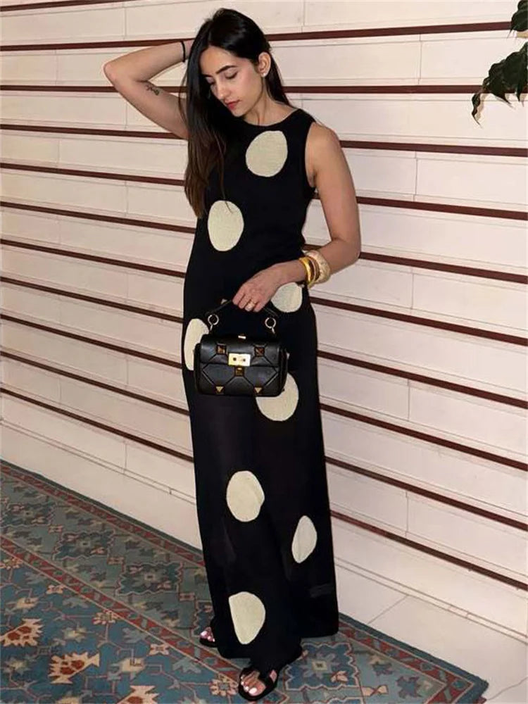 Woman in a black dress with white polka dots standing against a striped wall.