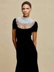 Woman wearing a black dress with an embellished neckline against a beige background