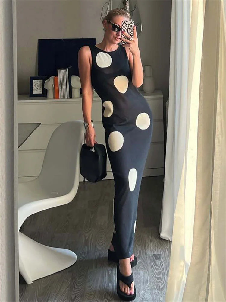 Woman in a black dress with white polka dots taking a mirror selfie in a room.