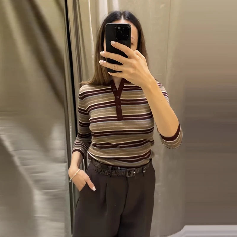 Person wearing a striped shirt and dark pants taking a mirror selfie.