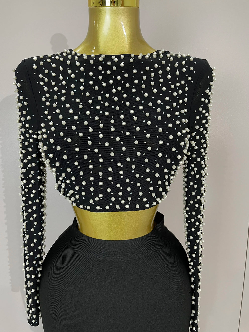 Black crop top with pearl embellishments on a mannequin against a plain background