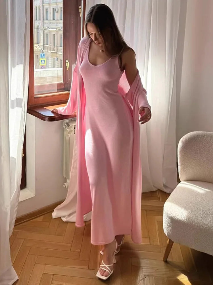 Woman in a pink dress standing in a room with a window and chair.