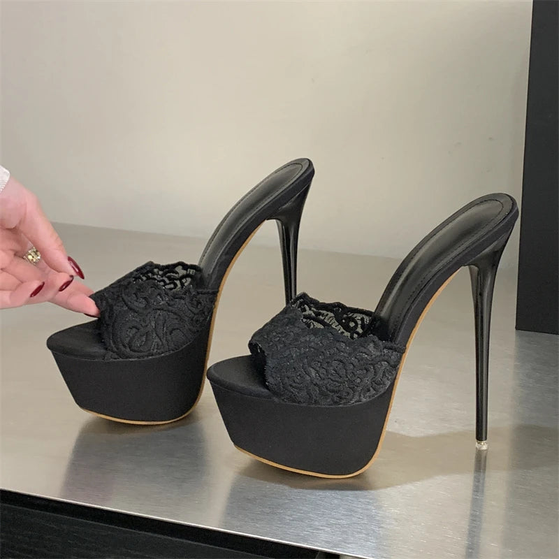Black high-heeled shoes with lace detailing on a reflective surface.