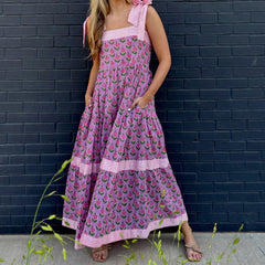 Woman wearing a pink floral dress against a dark brick wall.
