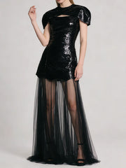 Black sequin mini dress with sheer tulle maxi overlay, model posing with arm raised.
