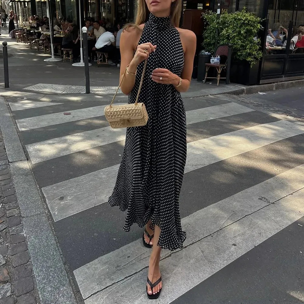 Woman in a black polka dot dress holding a straw bag on a city street.
