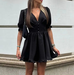 Woman wearing a black dress standing against a light-colored wall.