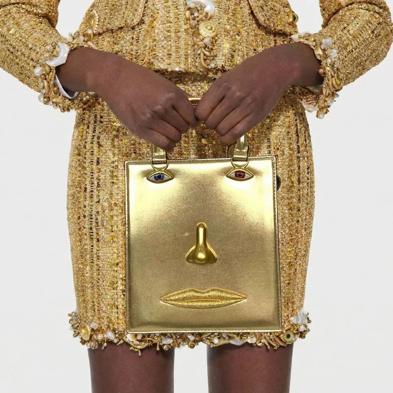 Gold sculptural face structured tote bag with top handle.