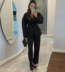 Woman taking a mirror selfie wearing a black suit in a room with a marble floor and white walls.