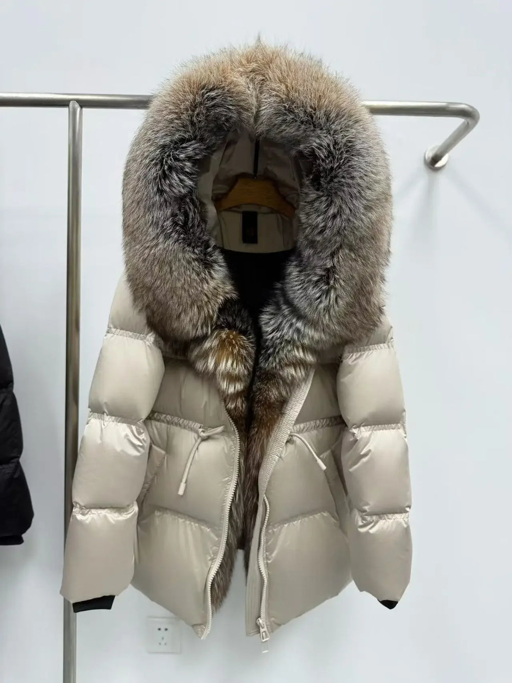 Beige puffer jacket with fur hood on a rack against a white background