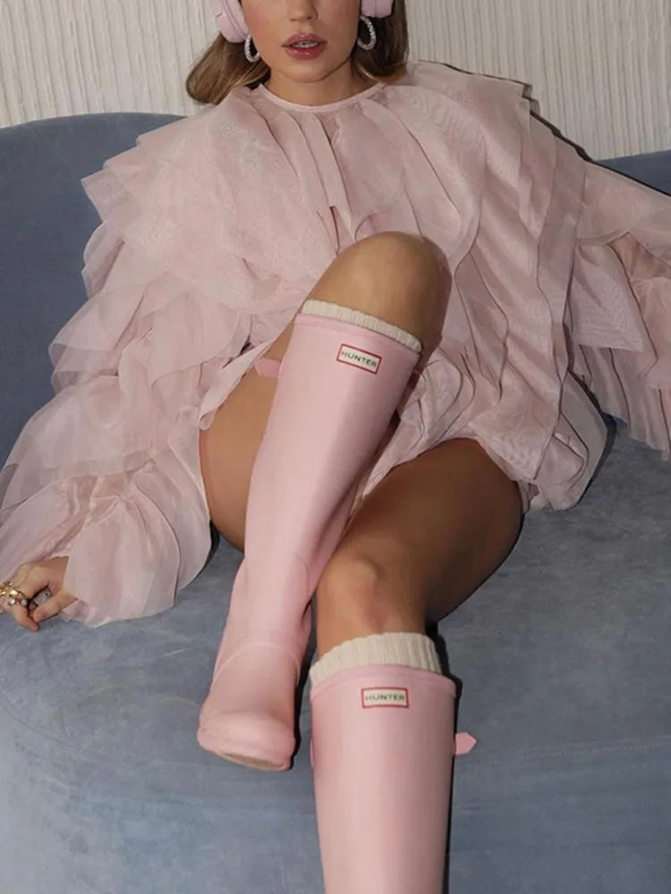 Person wearing pink Hunter boots sitting on a couch.