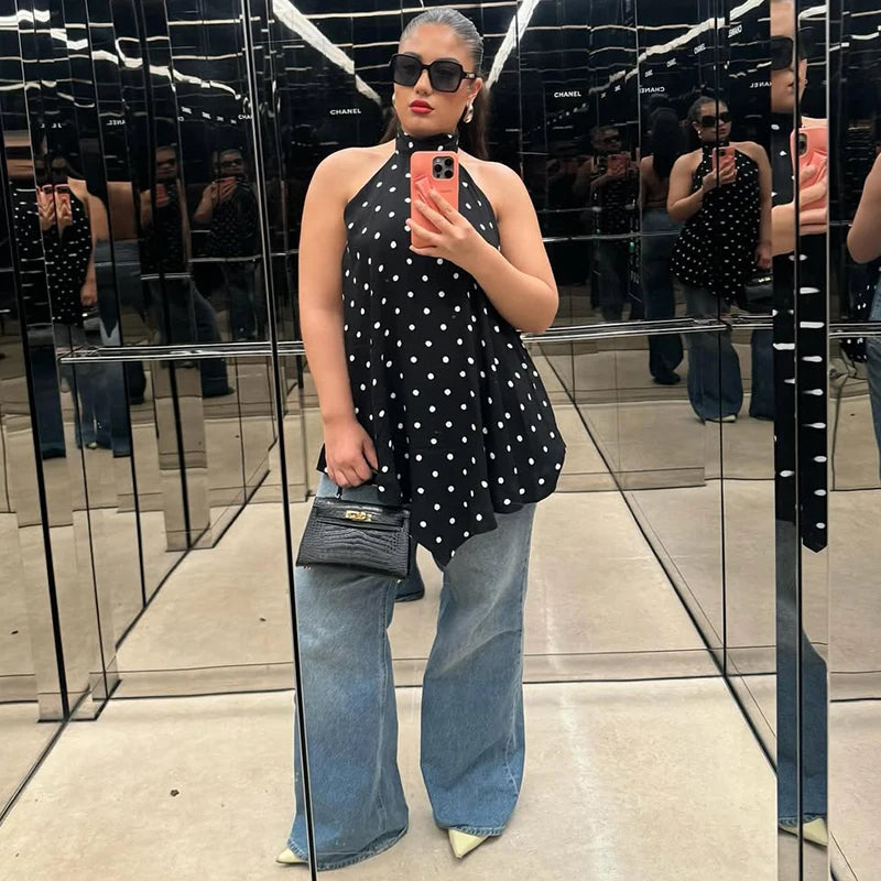 Woman taking a mirror selfie in a store, wearing a black polka dot top and blue jeans.