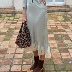 Person wearing a light-colored skirt with lace hem and holding a leopard print bag on a brick pavement.