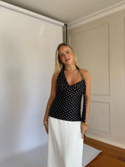 Woman wearing a black polka dot top and white pants standing indoors.