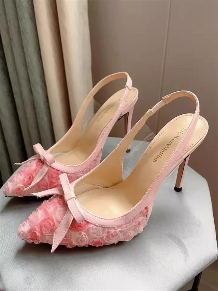 Pink lace high-heeled shoes with bows on a light surface.