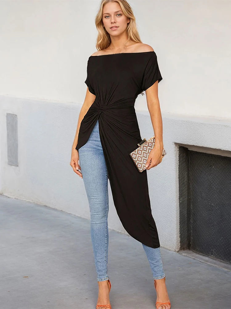 Woman wearing a black off-shoulder long top and blue jeans, standing against a plain background.