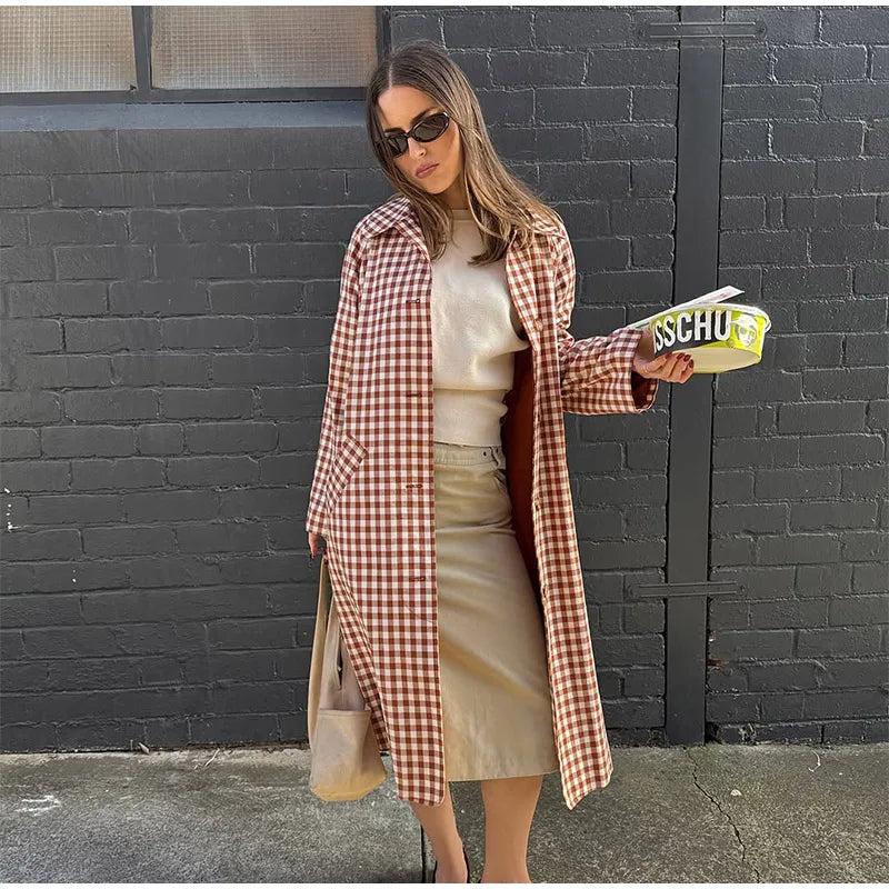 Woman in a plaid coat holding a magazine against a black brick wall.