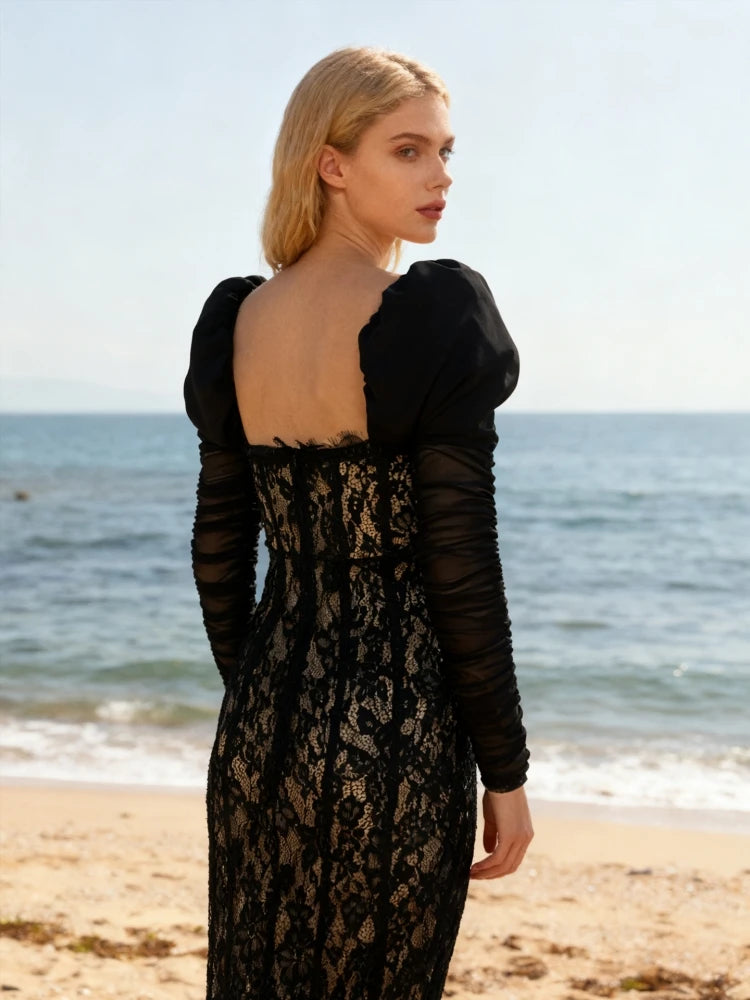 Woman in a black lace dress standing on a beach with ocean view