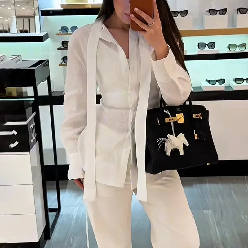 Person wearing a white outfit holding a black handbag with a horse emblem in a store setting.