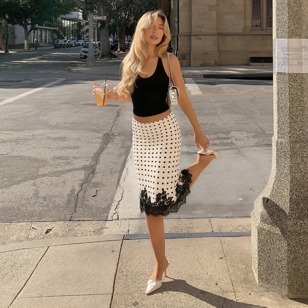 Woman walking on a city street wearing a black top and white skirt with black lace details.