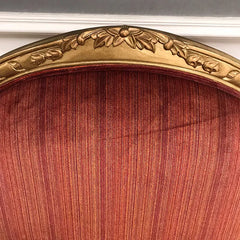 Close-up of a red velvet chair with a gold decorative frame.