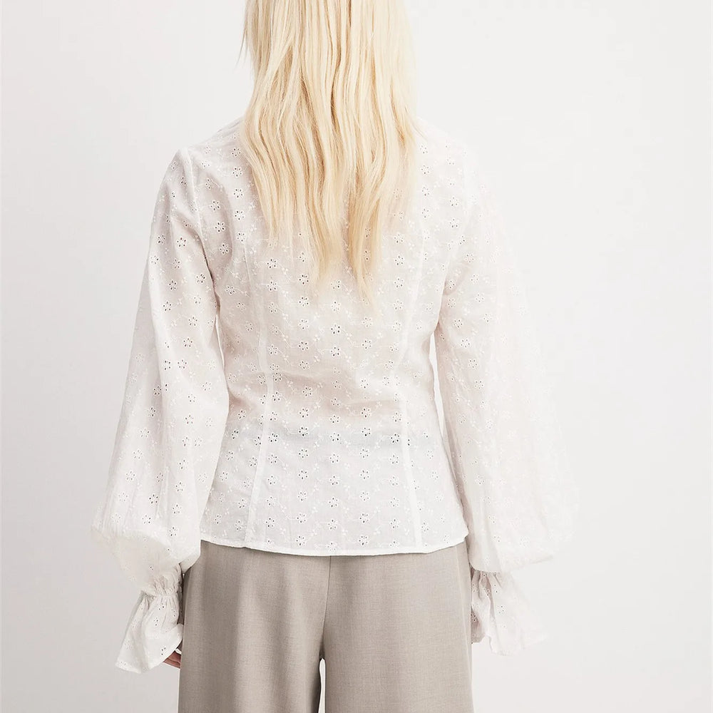 Person wearing a light-colored blouse with long sleeves on a plain background