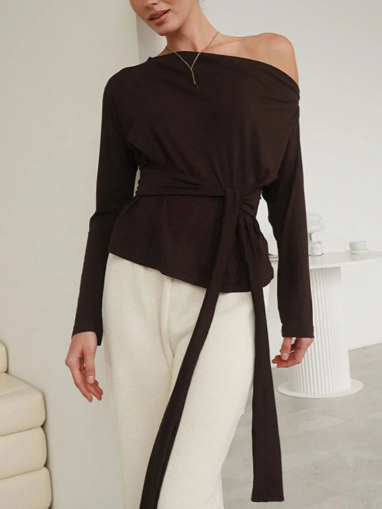 Woman wearing a black off-shoulder top with a tie detail in a minimalistic room.