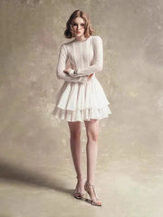 Woman wearing a white dress with long sleeves against a textured beige background